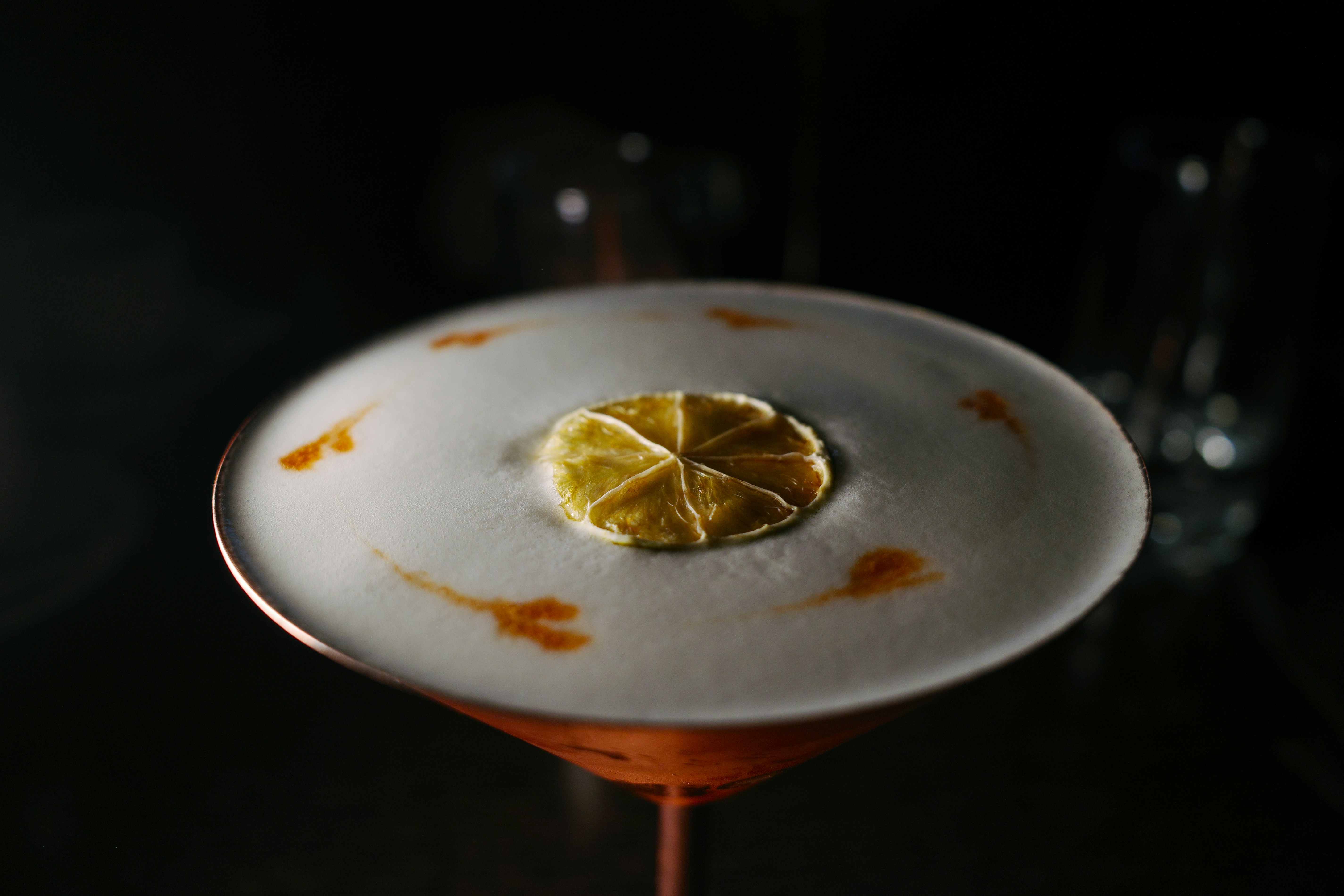 A bright foam cocktail coupe with a dehydrated citrus garnish